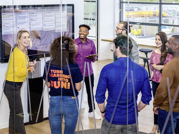 Foto von einem Meeting. Die Gruppe steht um ein interaktives Display.